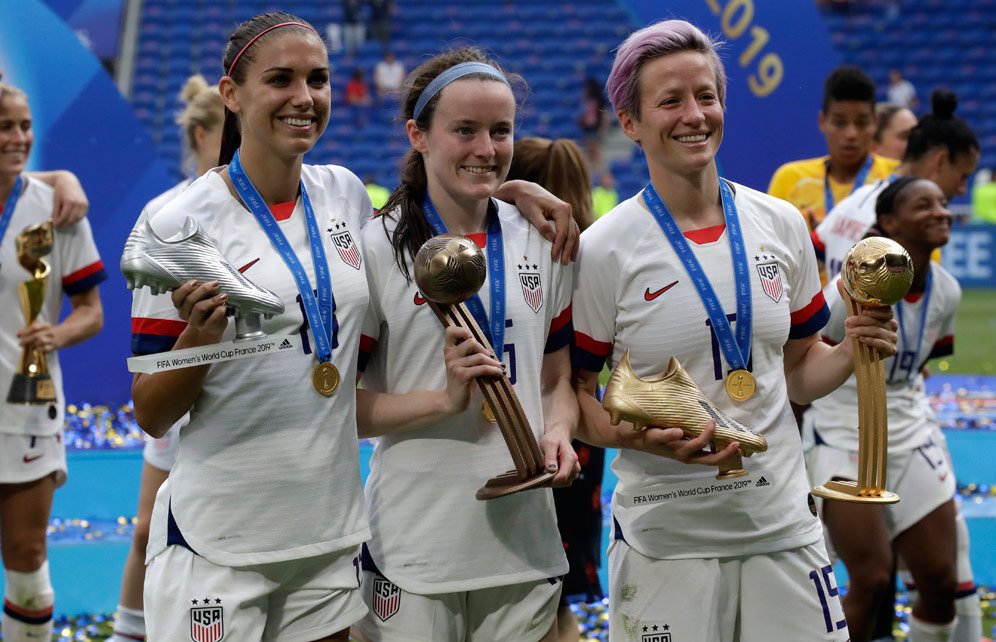 Megan Rapinoe (kanan), Alex Morgan (kiri) dan Rose Lavelle (tengah) berpose dengan trofi individu yang mereka raih di Piala Dunia Wanita 2019. (c) AP Photo