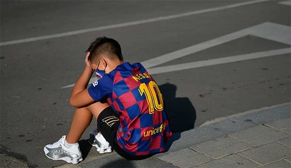 Seorang bocah tertunduk lesu saat menunggu Lionel Messi di lokasi latihan Barcelona, Senin (31/8/2020). Messi secara mengejutkan tidak datang untuk mengikuti tes swab Covid19 yang dijadwalkan Barcelona. (c) AFP/Paul Barrena