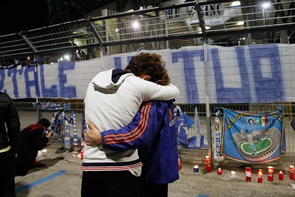 Dua suporter saling berpelukan di luar markas Napoli, San Paolo, setelah kabar meninggalnya Maradona. (c) AP Photo
