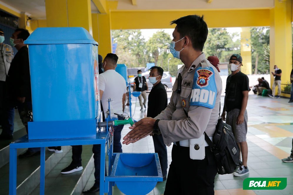 Seorang petugas kepolisian mencuci tangan sebelum melakukan swab antigen di Stadion Kanjuruhan, Malang, jelang pertandingan sepak bola Piala Menpora 2021, Senin (22/3/2021). (c) Bola.net/Arief Bagus