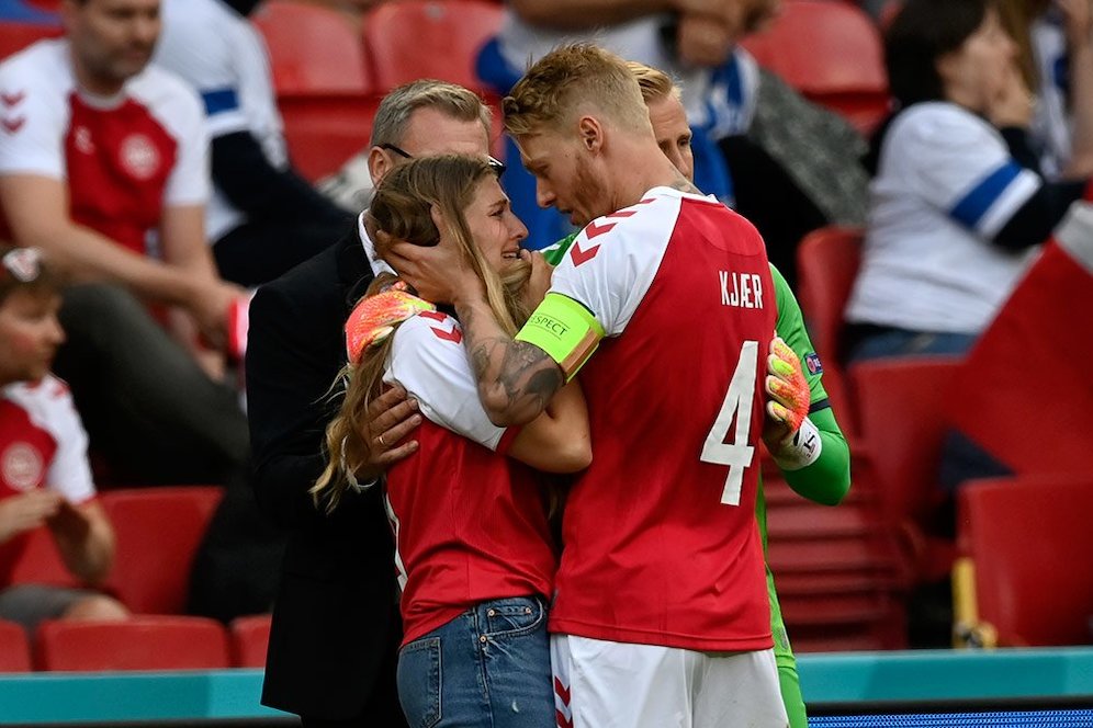 Bersama kiper Denmark, Kasper Schmeichel, kapten tim Simon Kjaer menecoba menenangkan Sabrina Kvist Jensen, istri Christian Eriksen. (c) AFP/Jonathan Nackstrand