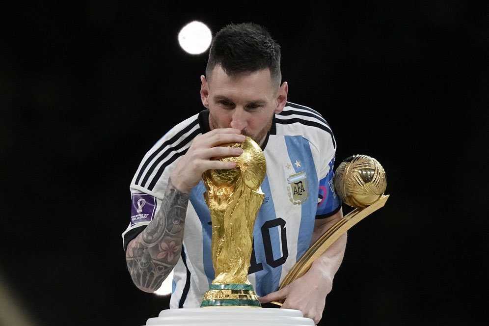Lionel Messi mencium trofi juara Piala Dunia 2022 Qatar usai membekuk Prancis di final, Minggu (18/12/2022). (c) AP Photo/Martin Meissner