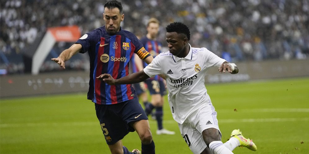Duel yang terjadi antara gelandang Barcelona, Sergio Busquets dengan penyerang sayap Real Madrid, Vinicius Junior pada final Supercopa de Espana 2023, Senin (16/1/2023) WIB. (c) AP Photo/Hussein Malla