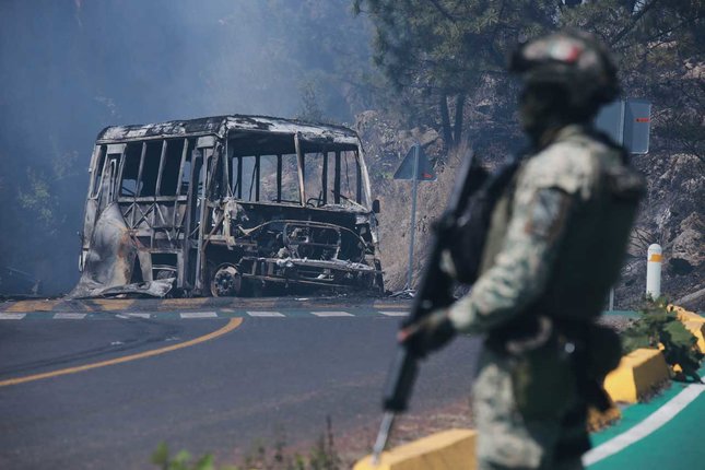 Seorang tentara berjaga di dekat kendaraan yang hangus terbakar di Cointzio, negara bagian Michoacan, Mexico, Minggu (22/2/2026), menyusul kematian El Mencho (c) AP Photo/Armando Solis
