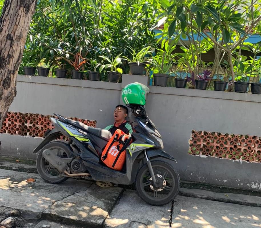 Driver ojol tampak pulas tertidur di pinggir jalan.