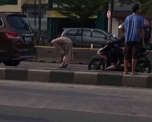 Seorang pria melakukan gerakan sholat di tengah jalan