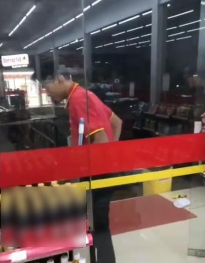 Karyawan minimarket sedang menyapu di luar.