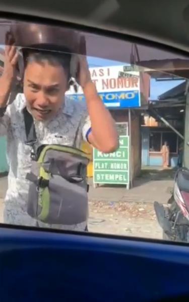 Pria itu tiba-tiba lepas helm dan menaruhnya di atas mobil.