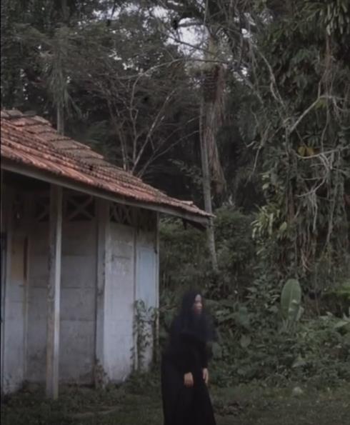 Gadis bergaun dan berkerudung hitam dekat rumah reyot pinggir hutan.