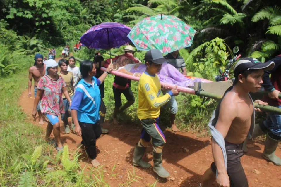 Warga desa Bahenap yang sakit harus rela digotong di siang hari sebelum menuju ke Rumah Sakit sejauh belasan kilometer karena akses jalan yang minim © Facebook.com/Selvianus Saludan