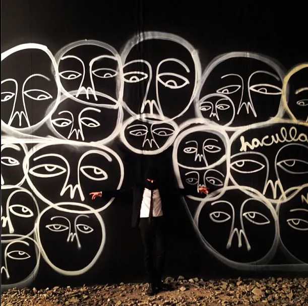 G-Dragon dengan gambar wajah di tembok gelap. ©soompi.com