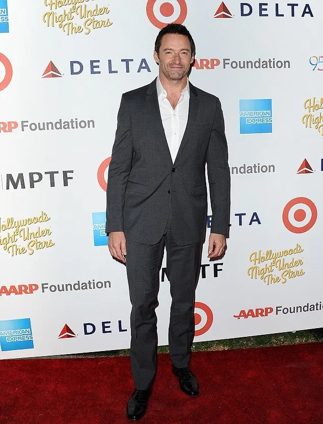 Memakai setelan jas dan kemeja putih, Hugh Jackman nampak memberikan senyum kepada kamera para fotografer yang mengambil gambarnya. © dailymailcouk