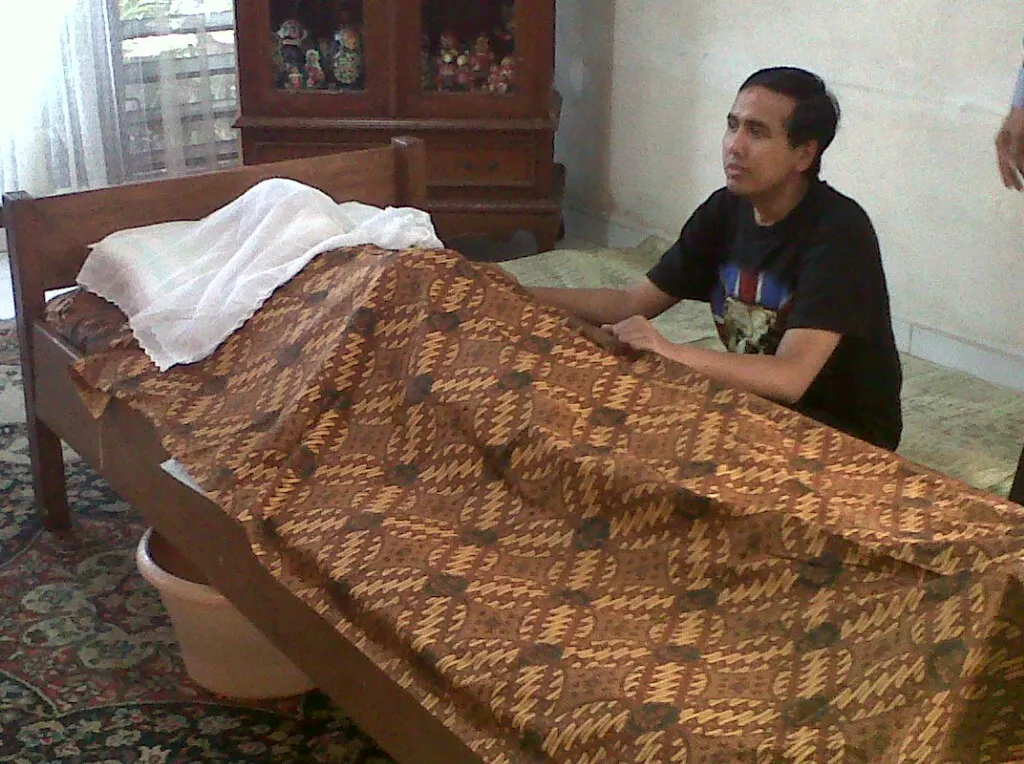 Gugun Gondrong menunggui jenazah ayahnya sebelum dimakamkan.