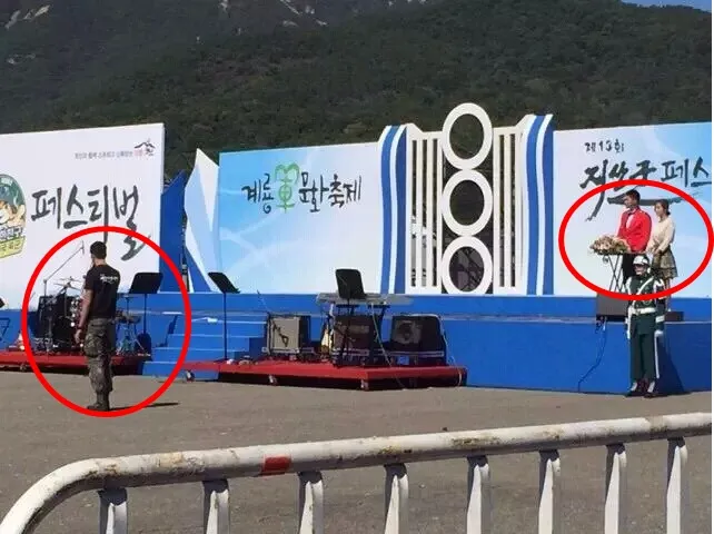 Yunho dalam seragam warna merah sebagai MC sedangkan Jaejoong berada di bawah panggung sambil membawa mic. ©soompi.com