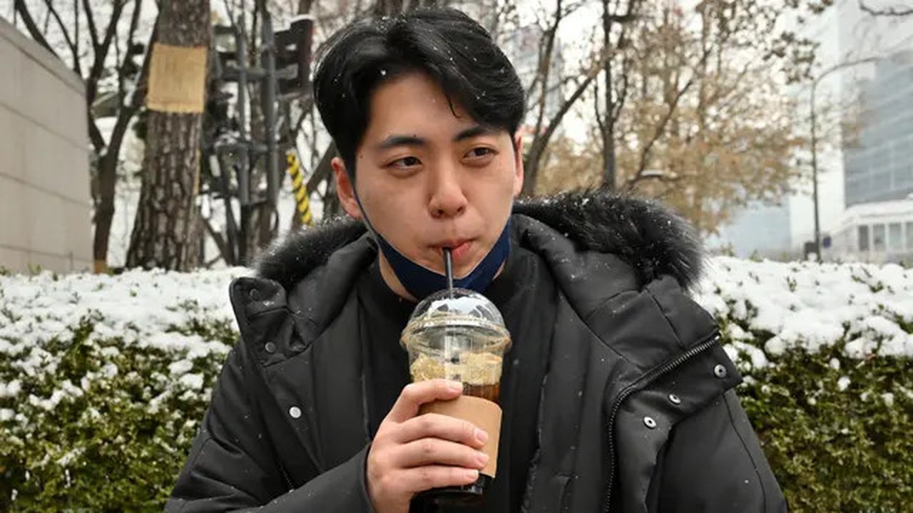 Gambar yang diambil pada 26 Januari 2023 ini menunjukkan akuntan Lee Dae-hee meminum es Americano selama wawancara dengan AFP di sebuah jalan di Seoul, Korea Selatan. Rata-rata orang Korea Se