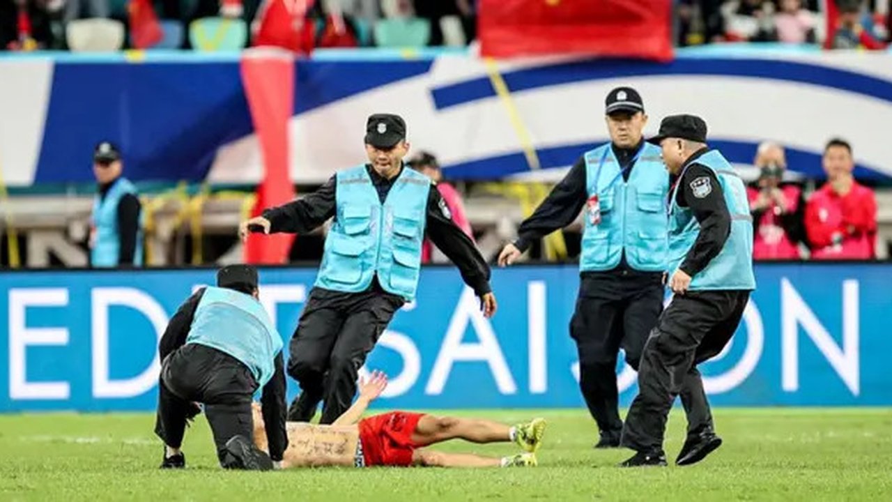Petugas keamanan berusaha mengawal seorang penggemar China yang menyerbu lapangan selama pertandingan kualifikasi Piala Dunia FIFA 2026 antara China dan Jepang di Xiamen, provins