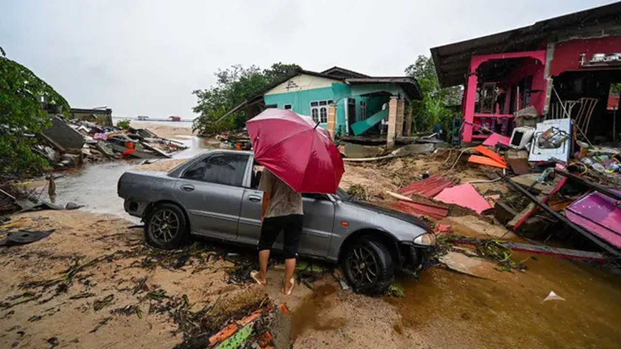 Seorang pria berjalan melewati sebuah mobil yang terdampar dan rumah-rumah yang rusak akibat banjir di Tumpat, negara bagian Kelantan, Malaysia, pada Rabu 4 Desember 2024. (MOHD RASFAN/AFP)