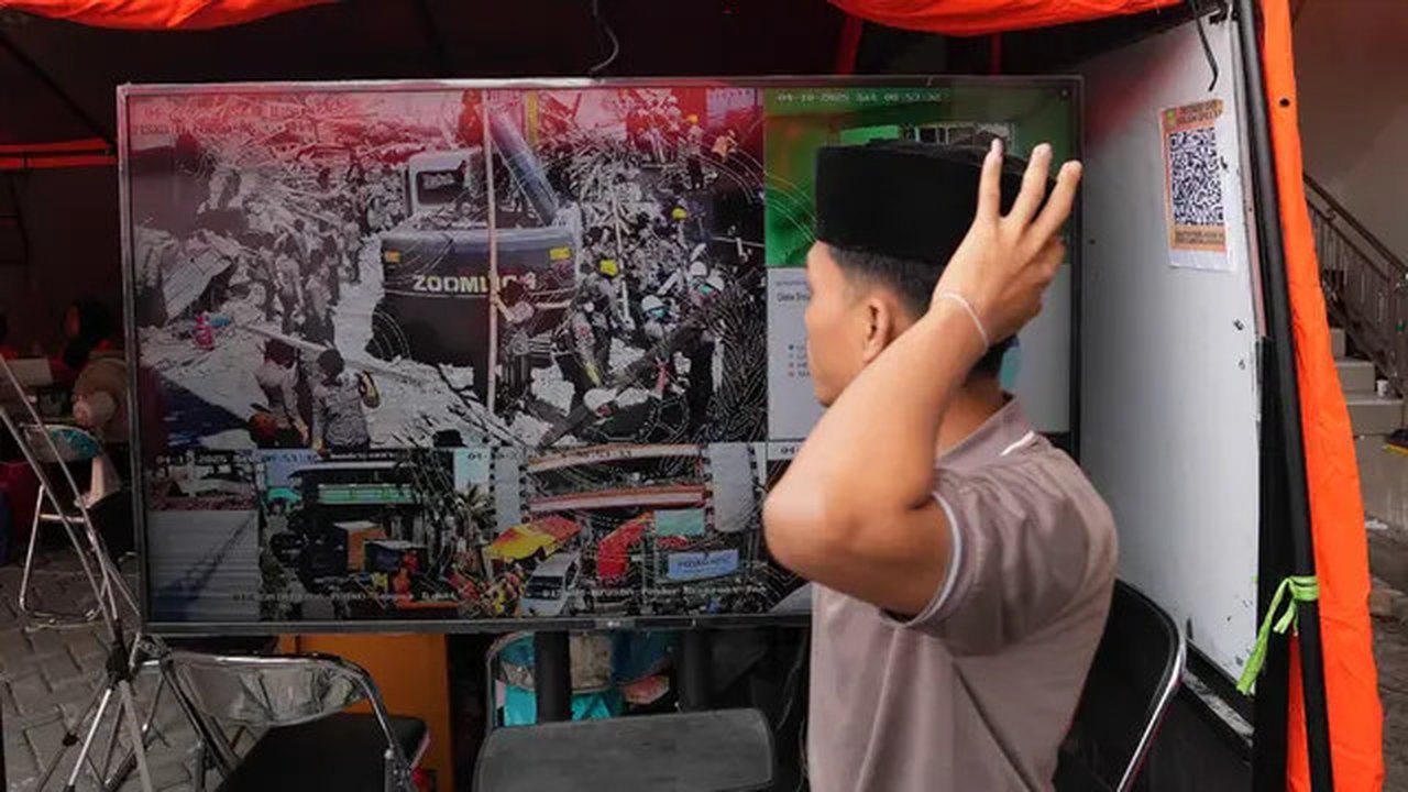 Seorang santri berjalan melewati layar TV yang menayangkan upaya pencarian korban hilang dari reruntuhan bangunan di sebuah pondok pesantren di Sidoarjo, Jawa Timur, Sabtu 4 Oktober 2025. (AP