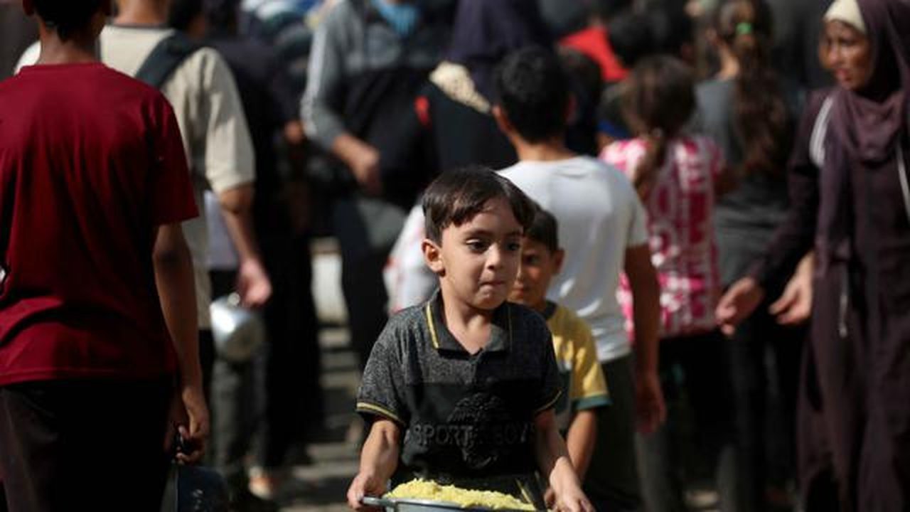 Seorang anak laki-laki Palestina yang sedang bermain membawa sepanci makanan yang ia terima dari sebuah tempat penampungan tempat tinggal keluarga-keluarga di Nuseirat, pusat Jalur Gaza, pada