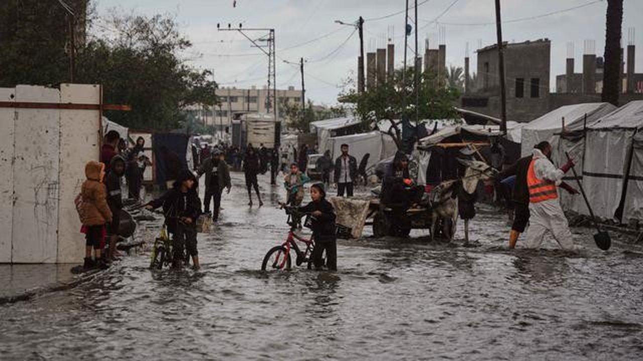 Warga Palestina berjalan di jalanan yang terendam banjir di samping kamp tenda sementara setelah hujan deras di Deir al-Balah, Jalur Gaza tengah, Selasa 25 November 2025. Banjir kembali mengg