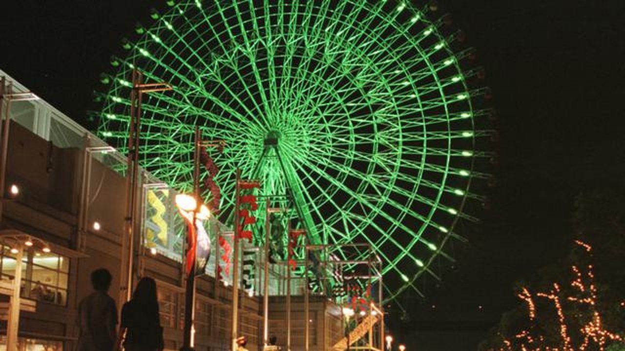 Sepasang kekasih berjalan melewati bianglala tertinggi di Jepang yang diterangi lampu di taman hiburan Tempozan Harbor Village di Osaka, pada akhir 11 Agustus 1997. Bianglala berdiameter 100