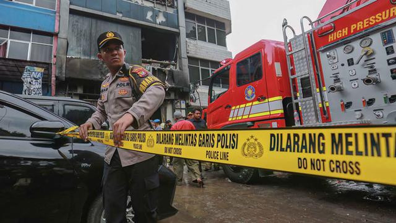 20 orang dilaporkan meninggal dunia dalam insiden tersebut. Api diduga berasal dari gudang baterai di lantai satu. Tampak dalam foto, seorang anggota kepolisian Indonesia memasang barikade un
