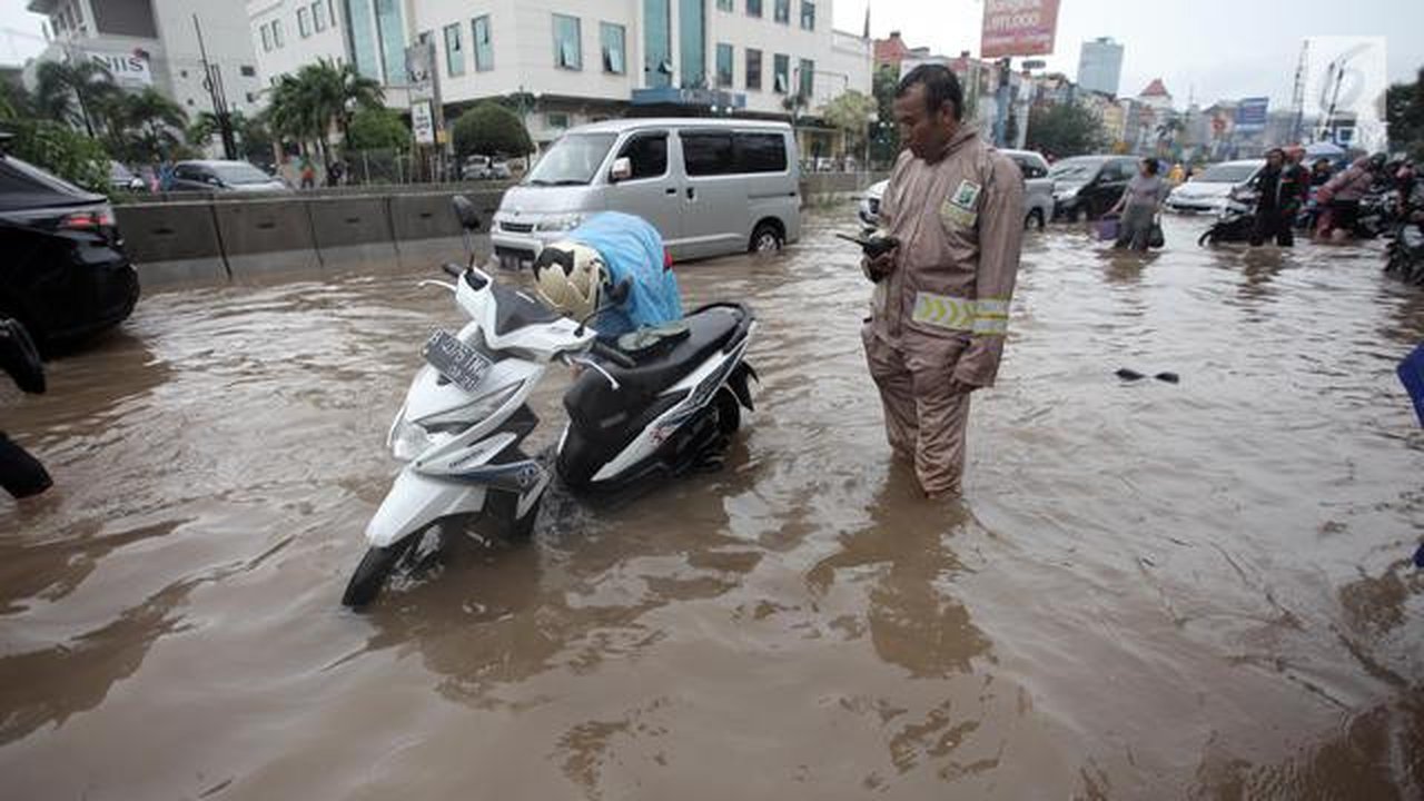 Seorang pengendara memperbaiki motornya yang mogok saat melintasi banjir di Jalan Boulevard Barat Raya, Kelapa Gading, Jakarta, Kamis (15/2). Hujan lebat yang mengguyur Jakarta mengakibatkan