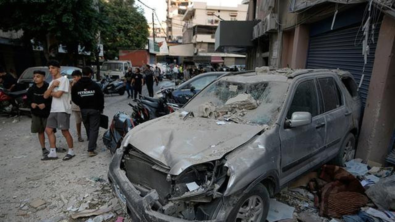 Orang-orang melintas di dekat sebuah mobil yang rusak di lokasi serangan Israel yang menghantam sebuah gedung apartemen di Dahiyeh, wilayah pinggiran selatan Beirut, Lebanon, Minggu, (23/11/2