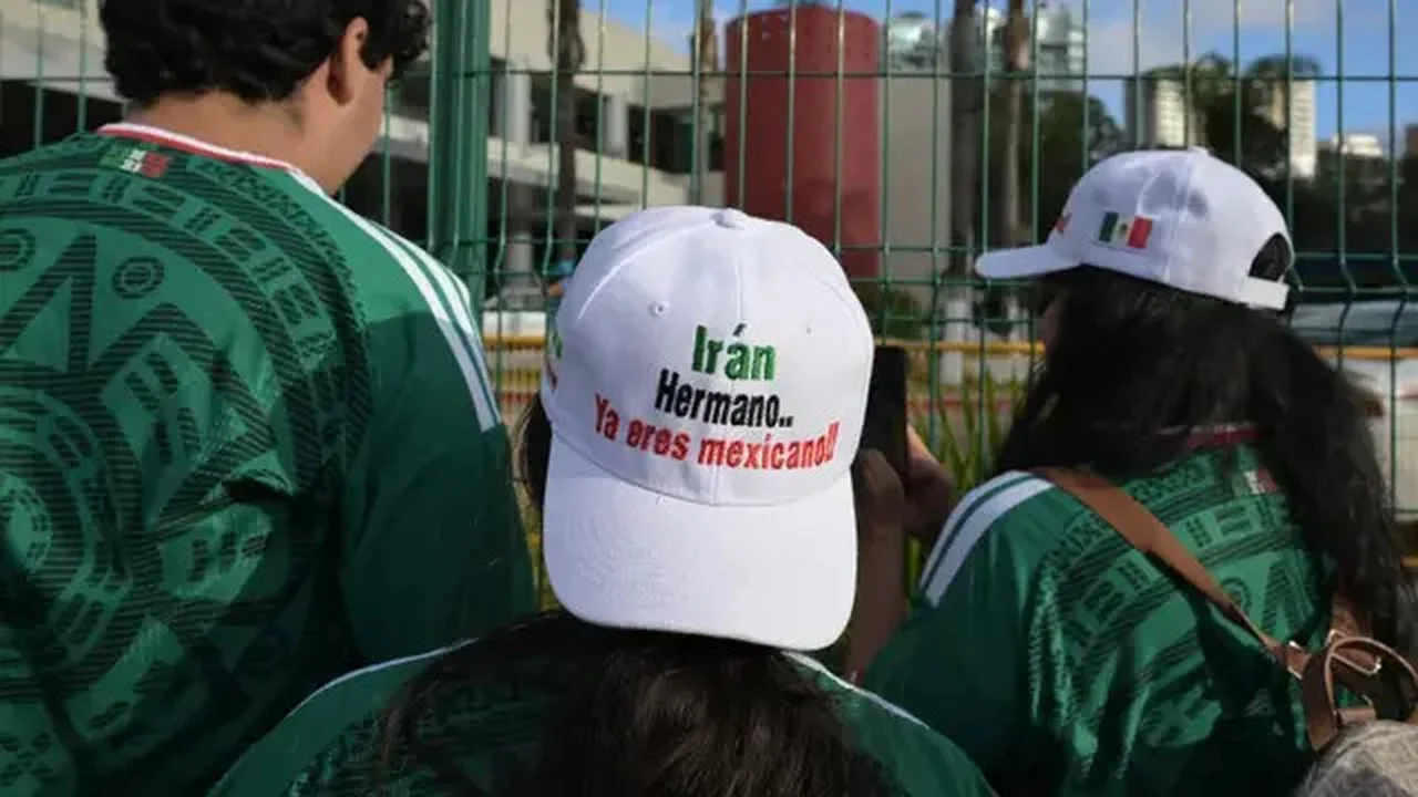Para penggemar sepak bola di Meksiko menunggu tim Iran sambil mengenakan topi bertuliskan, 'Iran, saudaraku, kau sekarang orang Meksiko', di luar hotel tim di Tijuana, Meksiko, pada 27 Juni 2