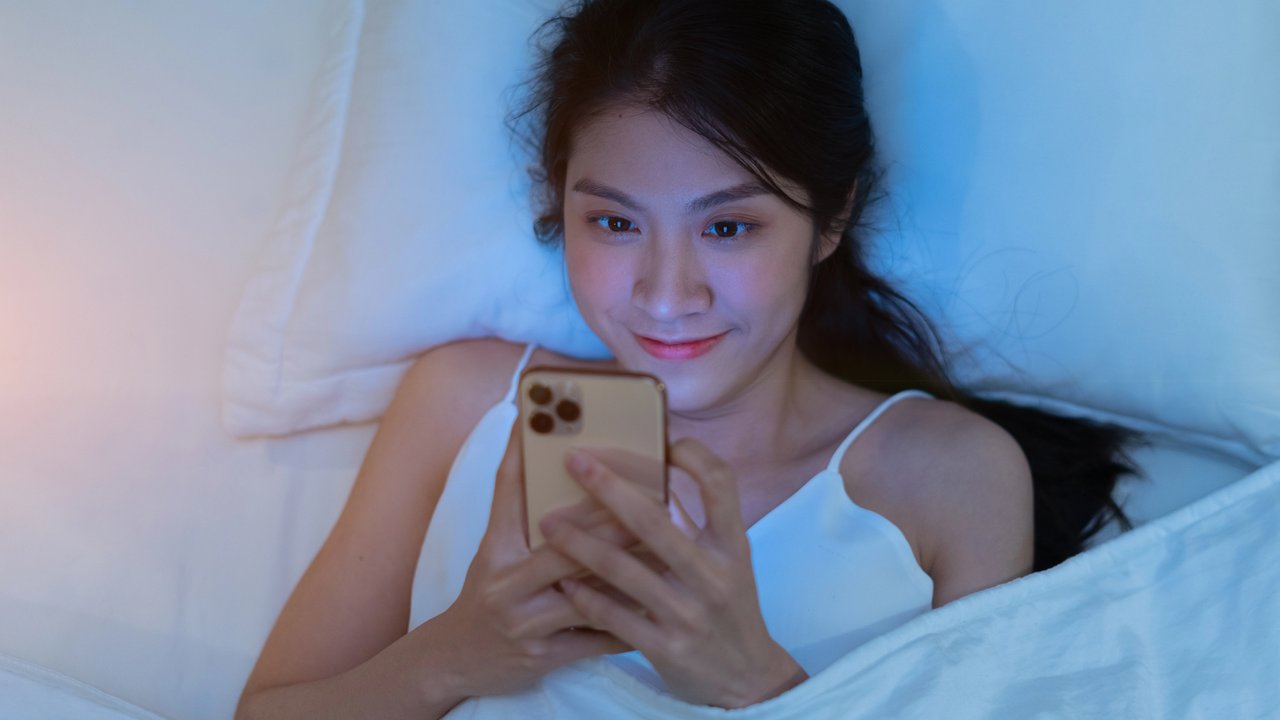 Ilustrasi perempuan dengan paparan blue light dari layar handphone.