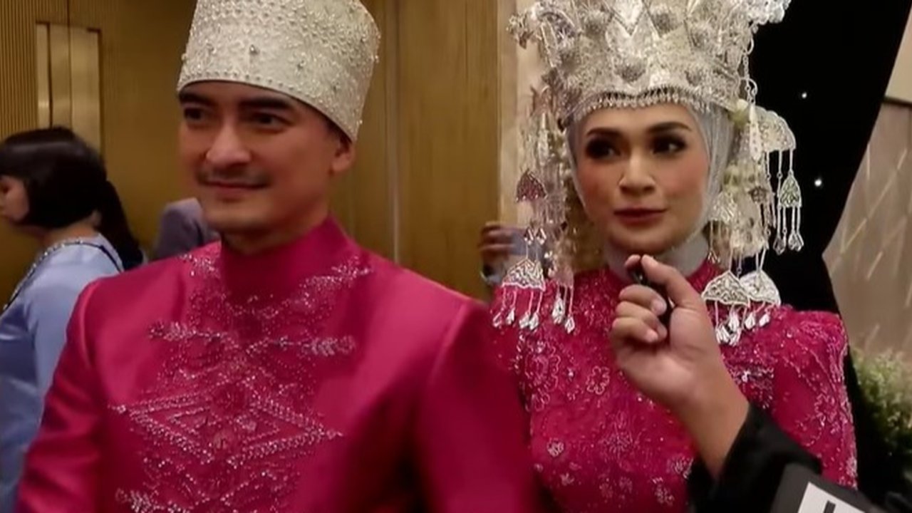 Pasangan pengantin pernikahan Zumi Zola & Putri Zulhas mengenakan baju adat warna pink yang cerah dengan hiasan kepala, yang diperkirakan merupakan baju adat pernikahan khas Jambi.