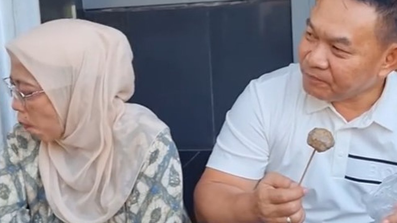 Dudung Abdurachman duduk santai sambil menikmati jajanan khas Jawa Barat cilok.