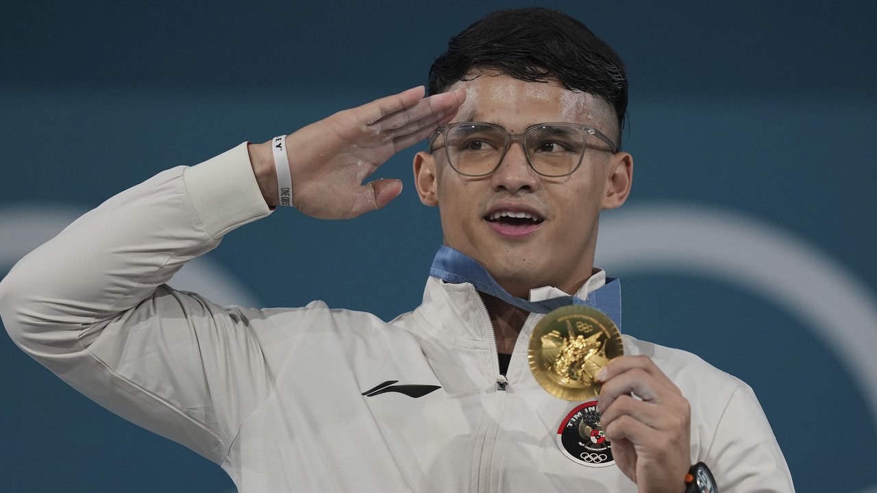 <p>Veddriq Leonardo menggigit medali emas Olimpiade Paris 2024 usai tiba di Bandara Internasional Soekarno-Hatta, Tangerang, Selasa (13/08/2024). (Abdul Aziz/Bola.com)</p>