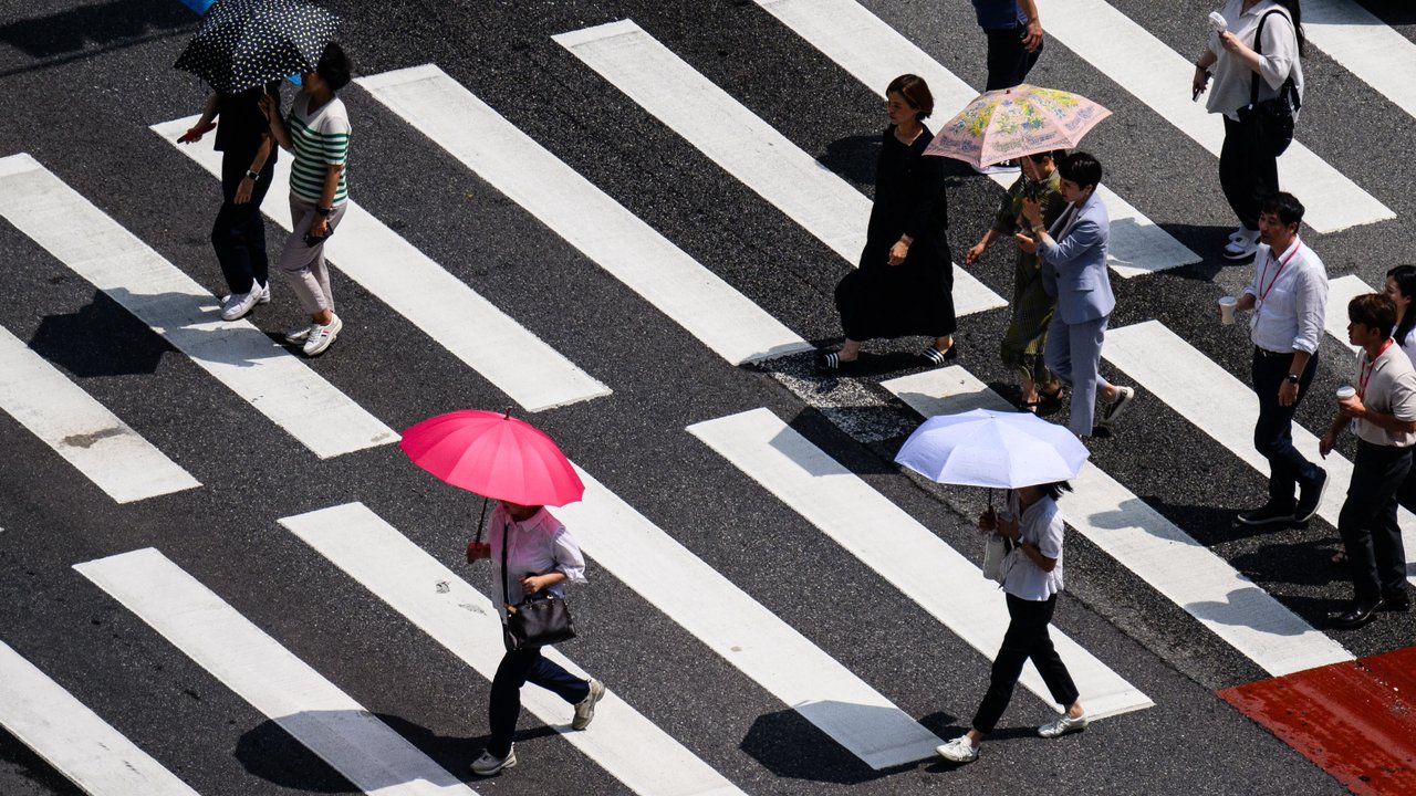 Pejalan kaki menggunakan payung saat menyeberangi jalan di Seoul pada tanggal 14 Agustus 2024. (Anthony WALLACE/AFP)