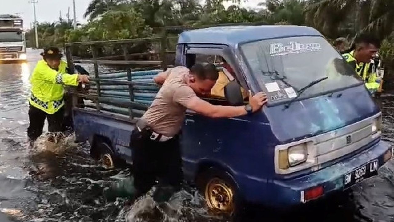 Personel Lalu Lintas Polres Pelalawan mendorong mobil mogok karena banjir di Jalan Lintas Timur Sumatra. (Liputan6.com/M Syukur)