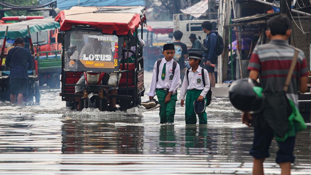 Warga melewati banjir rob yang merendam kawasan Muara Baru, Jakarta Utara, Selasa (14/1/2025).