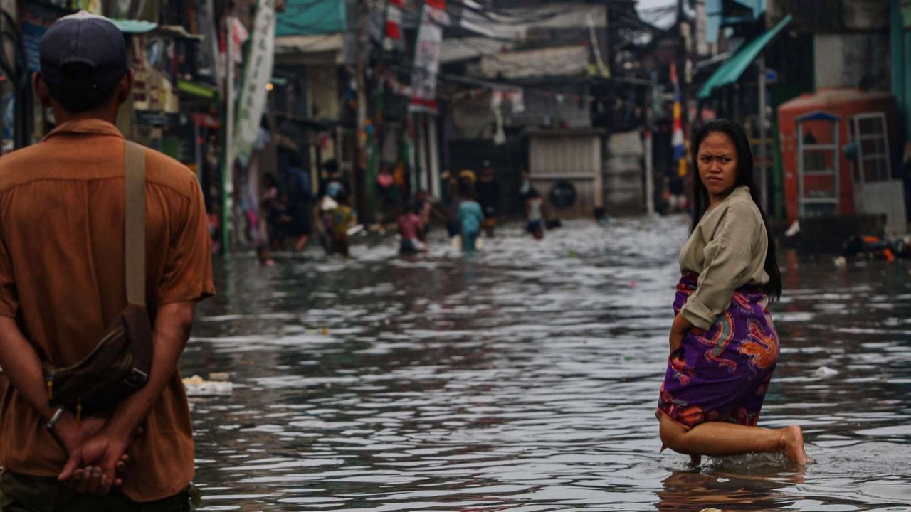 Warga melewati banjir rob yang merendam kawasan Muara Baru, Jakarta Utara, Selasa (14/1/2025).