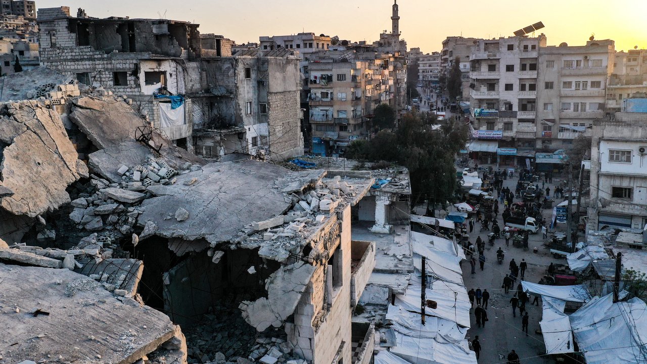 Orang-orang berjalan melewati bangunan yang runtuh di