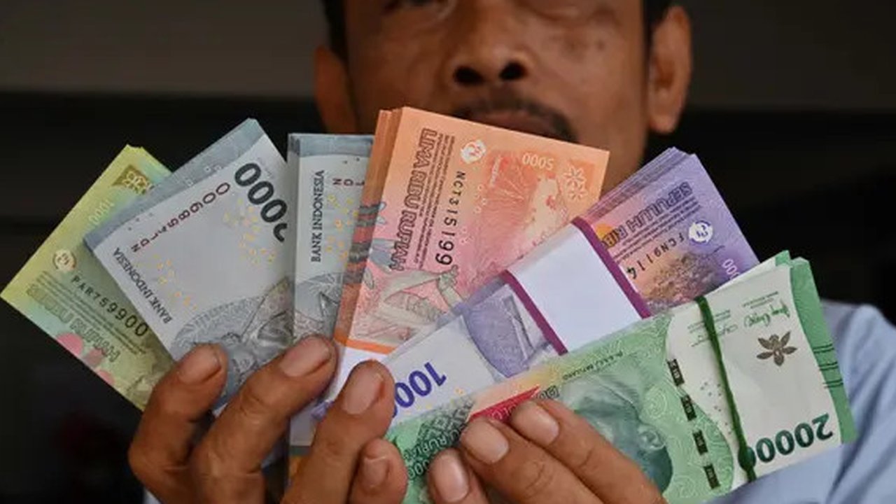 Seorang pria menunjukkan uang kertas Rupiah yang baru, yang akan diberikan kepada anggota keluarganya saat perayaan Idul Fitri, di Jakarta pada 28 Maret 2024. (Adek BERRY/AFP)