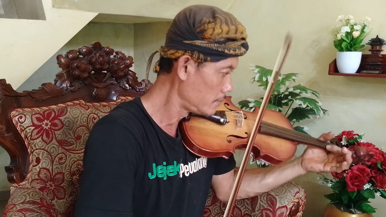 Potret Mbah Min memainkan alat musik gesek, biola yang diproduksinya.