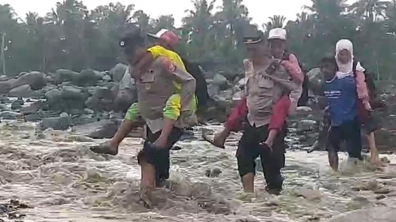 Anggota Polsek Candipuro membantu pelajar menyeberangi sungai aliran lahar di Desa Jugosari untuk pergi ke sekolah