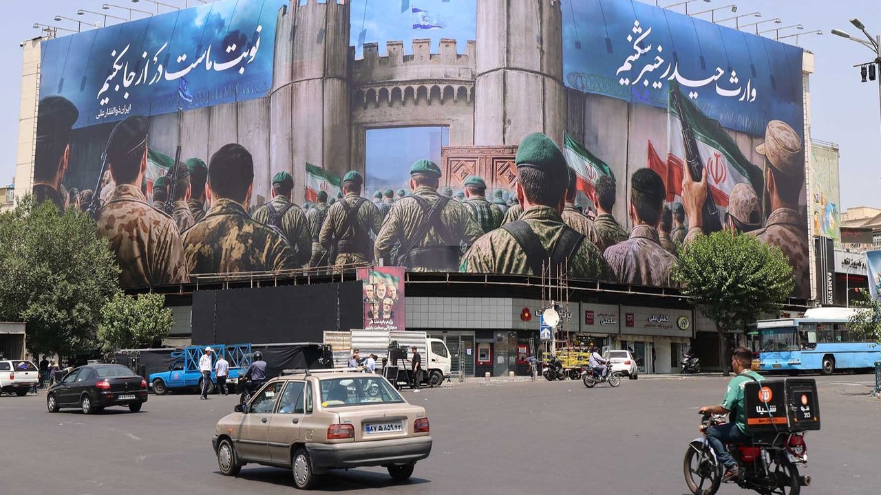 Seorang pria mengendarai sepeda motornya di samping poster anti-Israel di Teheran, Sabtu (14/06/2025).