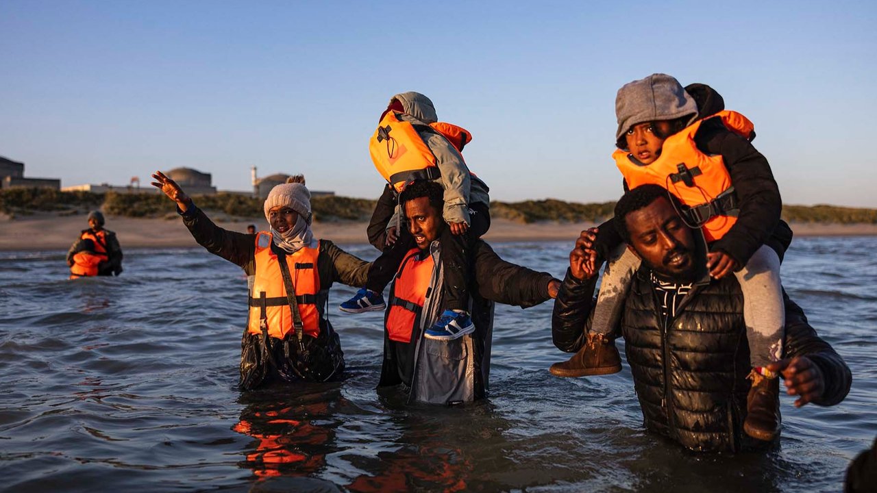 Para migran menggendong anak-anak mereka saat berjalan di air untuk menaiki perahu penyelundup dalam upaya menyeberangi Selat Inggris di lepas pantai Gravelines, Prancis utara, (16/06/2025).