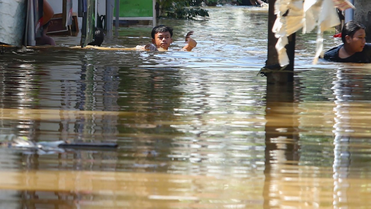 Warga beraktifitas saat banjir merendam pemukiman di Jalan Pirus, Kelurahan Bidara Cina, Jatinegara, Jakarta Timur, Minggu (06/07/2025).