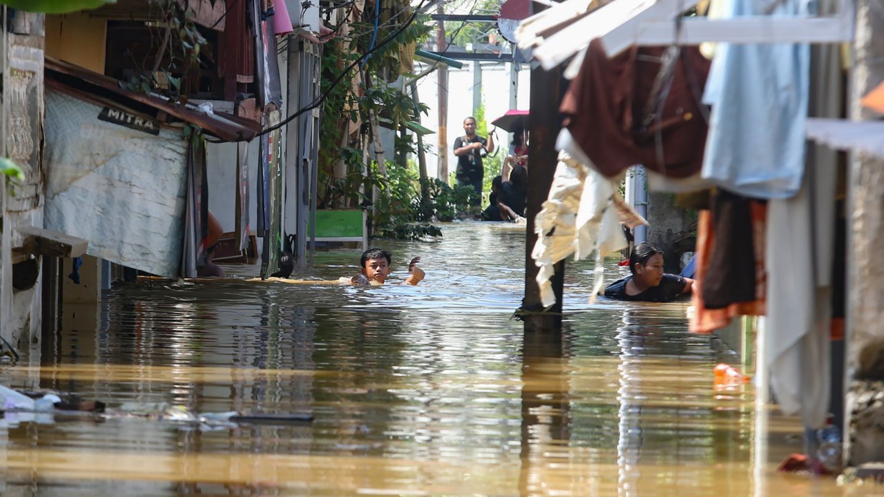 Warga beraktifitas saat banjir merendam pemukiman di Jalan Pirus, Kelurahan Bidara Cina, Jatinegara, Jakarta Timur, Minggu (06/07/2025).