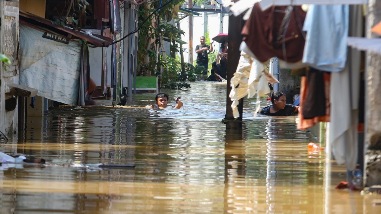 Warga beraktifitas saat banjir merendam pemukiman di Jalan Pirus, Kelurahan Bidara Cina, Jatinegara, Jakarta Timur, Minggu (06/07/2025).