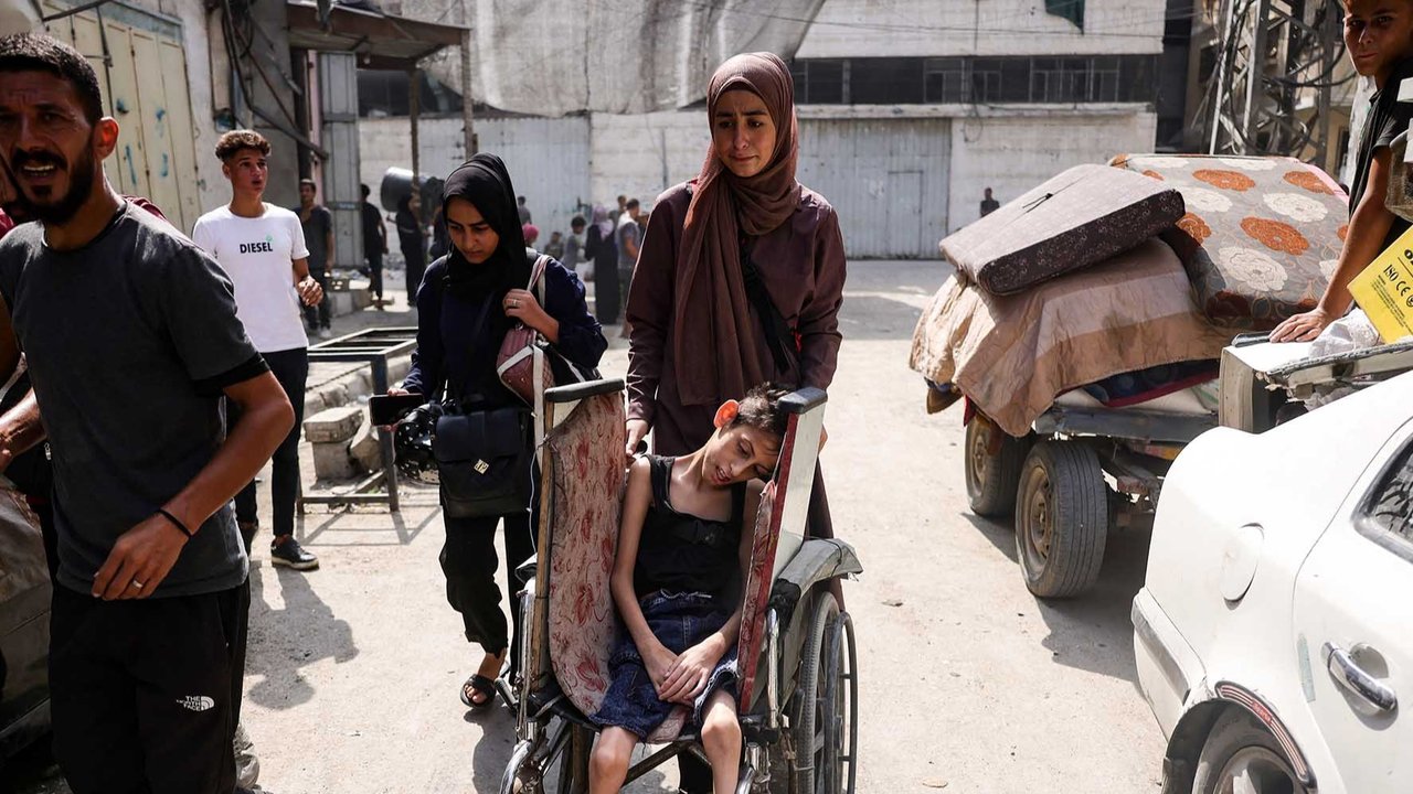Seorang perempuan Palestina mendorong kursi roda anaknya saat ia mengungsi  bersama warga lain dari permukiman Abu Iskandar di utara Kota Gaza, Palestina, Jumat (22/08/2025).