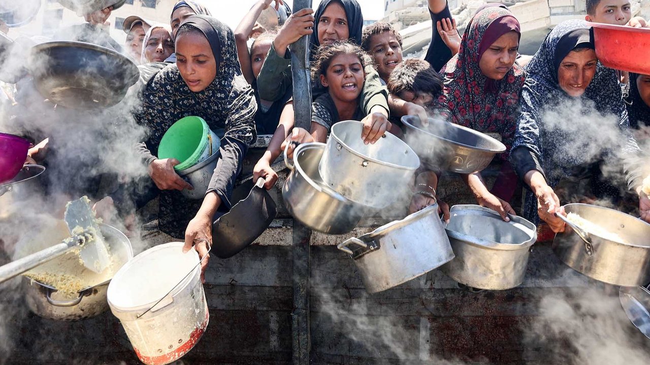 Warga Palestina mengulurkan panci kosong mereka untuk menerima nasi dari dapur amal di Kota Gaza, Sabtu (23/08/2025).