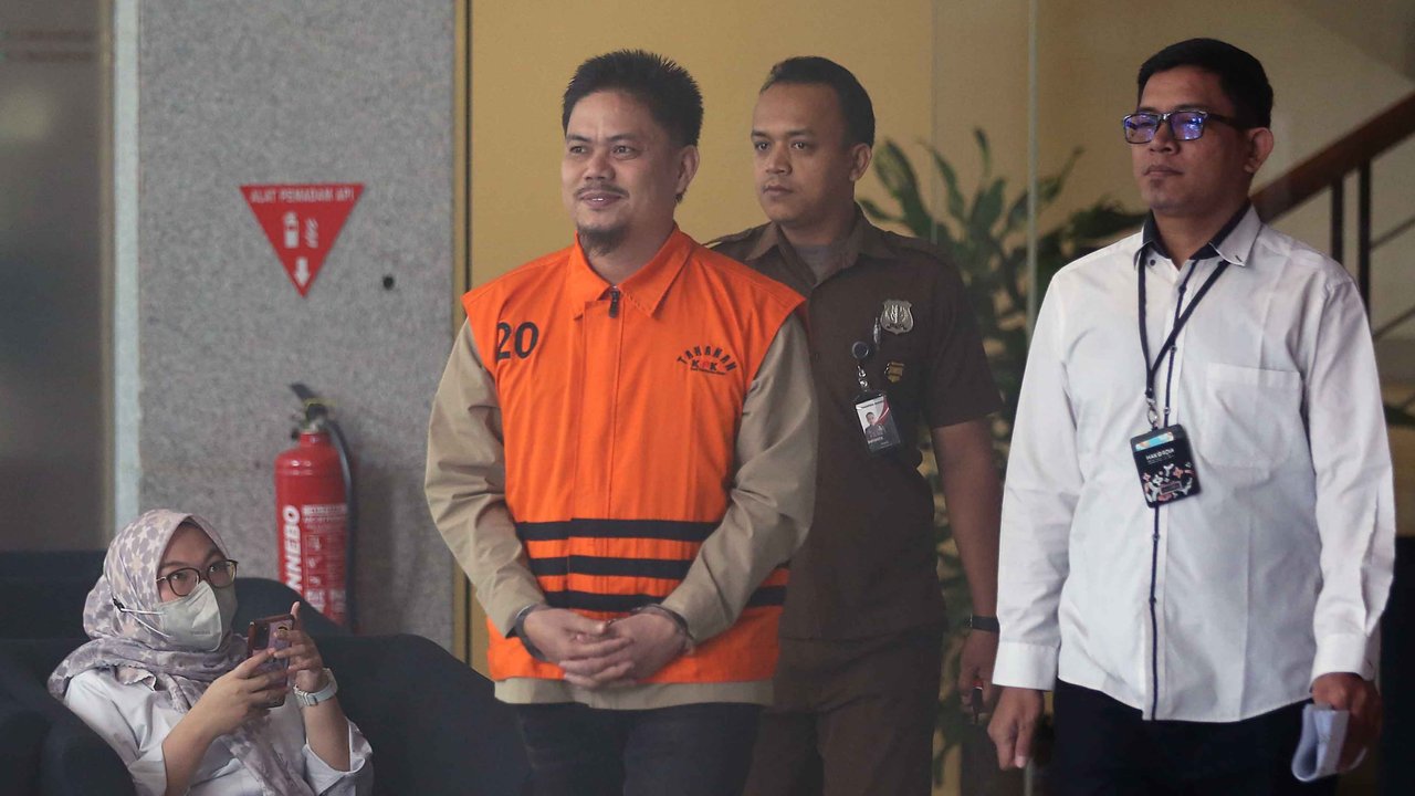 Bupati nonaktif Kolaka Timur Abdul Aziz dengan memakai rompi KPK dan tangan diborgol berjalan keluar usai menjalani pemeriksaan di Gedung Merah Putih Komisi Pemberantasan Korupsi, Jakarta, Rabu (27/8/2025). 
Liputan6.com/Helmi Fithriansyah