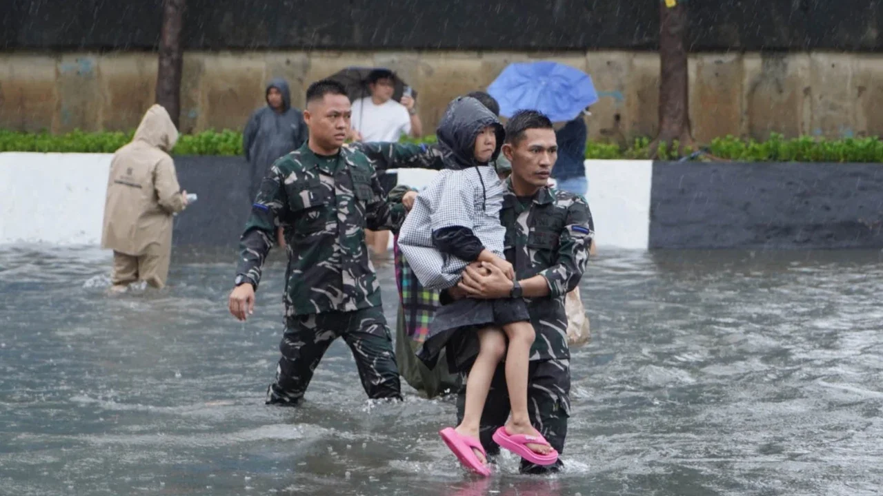 Prajurit TNI Angkatan Laut membantu warga melintasi banjir di Jalan Raya Pademangan, Jakarta Utara. Senin (12/01/2026)